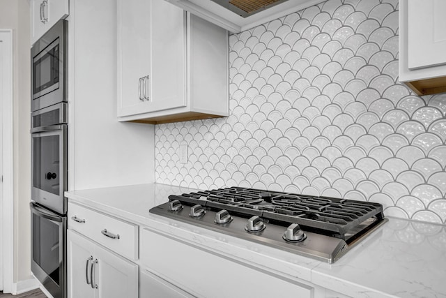 kitchen featuring appliances with stainless steel finishes, white cabinetry, backsplash, and light stone countertops