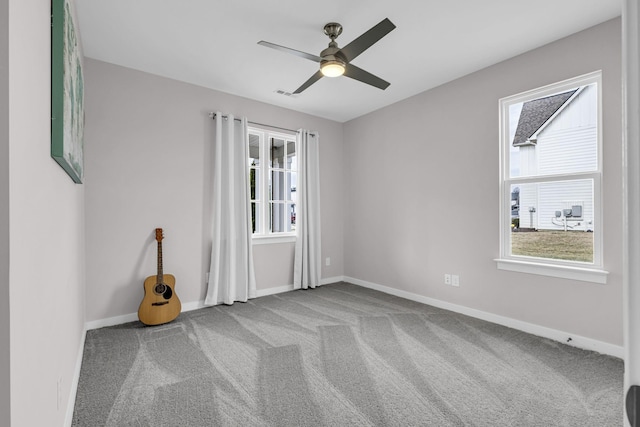 carpeted empty room with ceiling fan, a wealth of natural light, and baseboards