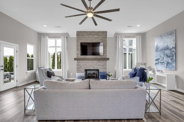 living room with a wealth of natural light, a stone fireplace, and wood finished floors