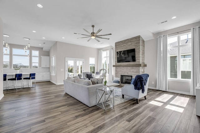 living area with plenty of natural light, visible vents, wood finished floors, a stone fireplace, and french doors