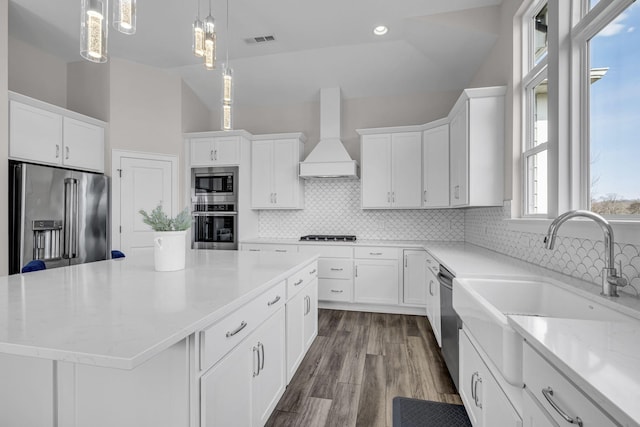 kitchen with visible vents, a kitchen island, custom exhaust hood, stainless steel appliances, and white cabinetry