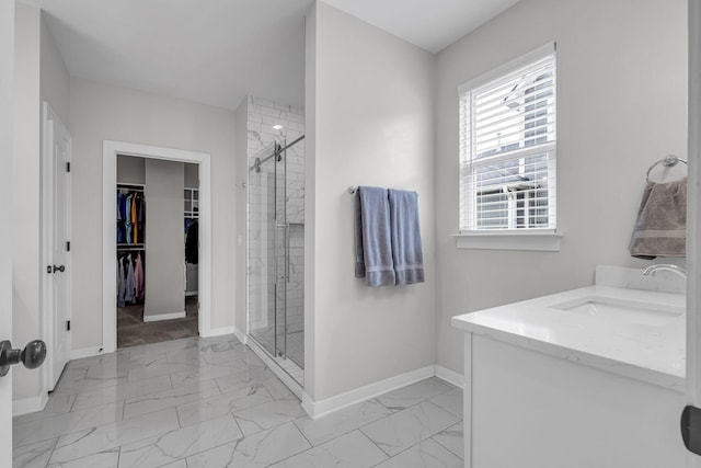 bathroom featuring marble finish floor, a shower stall, a spacious closet, and baseboards