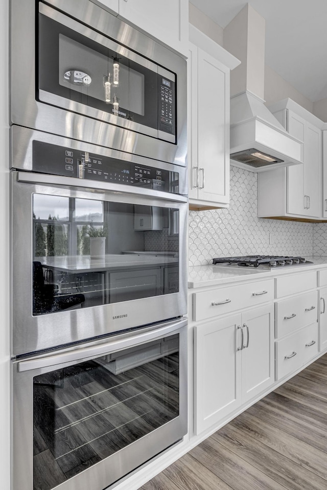 kitchen featuring tasteful backsplash, white cabinets, appliances with stainless steel finishes, light countertops, and premium range hood