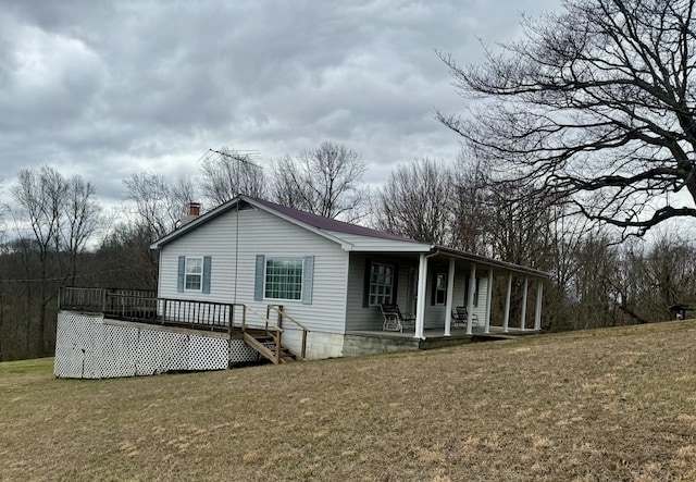 back of house featuring covered porch, a chimney, and a lawn