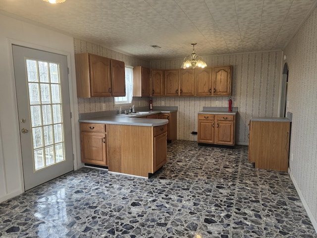 kitchen with brown cabinetry, a sink, a peninsula, and wallpapered walls