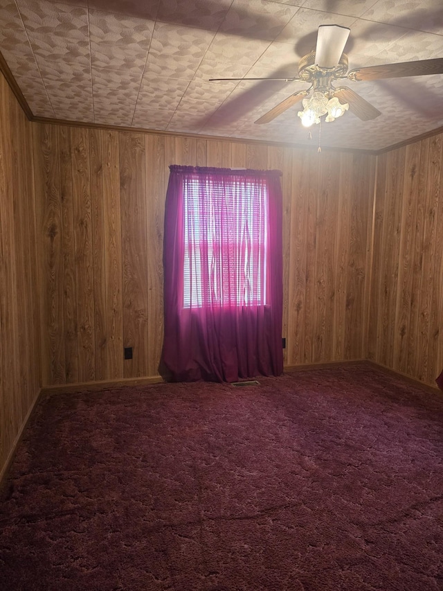 spare room featuring wood walls, a ceiling fan, and carpet flooring