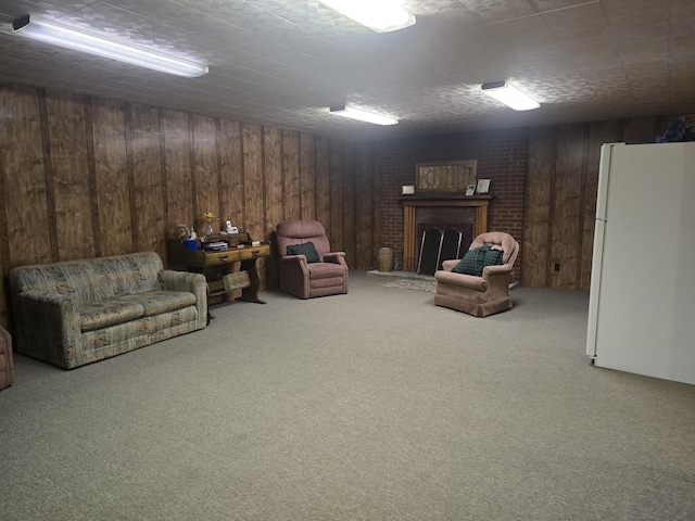 finished below grade area featuring wooden walls, carpet, freestanding refrigerator, and a brick fireplace