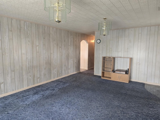 unfurnished living room featuring baseboards, wooden walls, arched walkways, and dark colored carpet