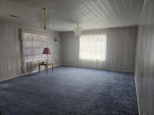 carpeted spare room with wood walls, baseboards, and visible vents