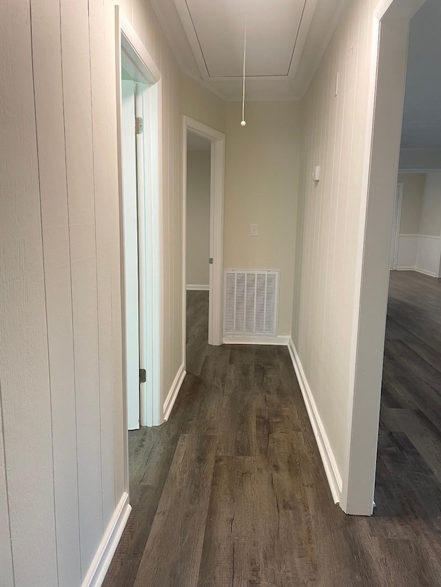 corridor with attic access, visible vents, dark wood finished floors, baseboards, and ornamental molding