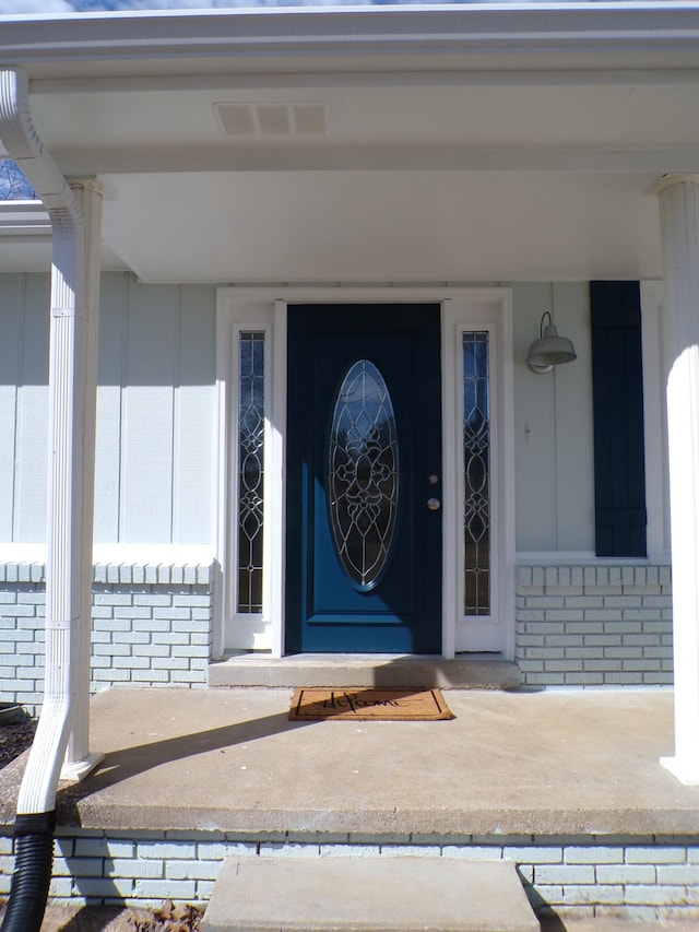 doorway to property with covered porch, brick siding, and visible vents