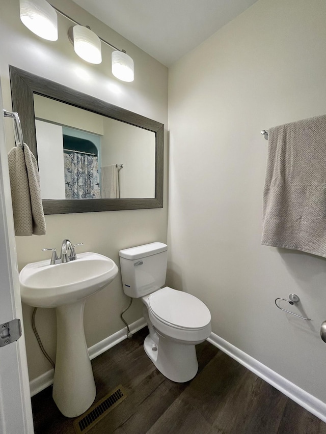 bathroom with visible vents, toilet, a sink, wood finished floors, and baseboards