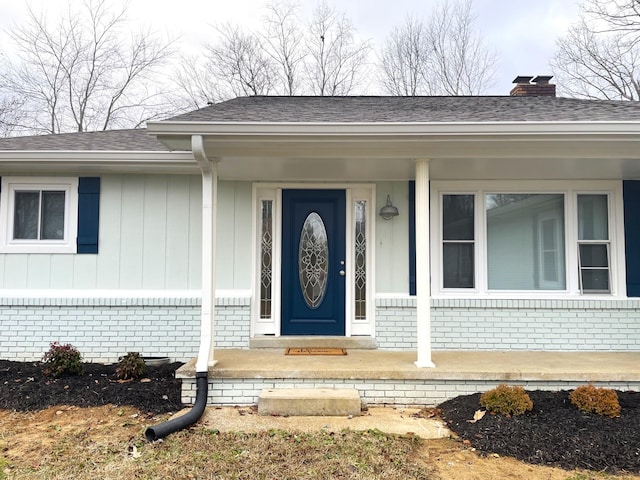 doorway to property featuring a shingled roof, brick siding, and a chimney