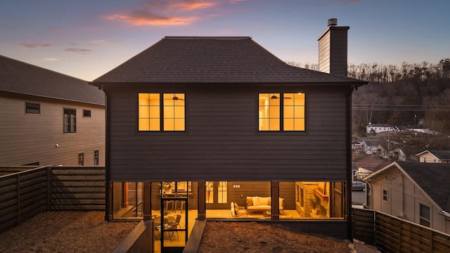 back of house at dusk with a fenced backyard, a patio, and a chimney