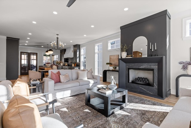 living room featuring a premium fireplace, ornamental molding, wood finished floors, a chandelier, and recessed lighting