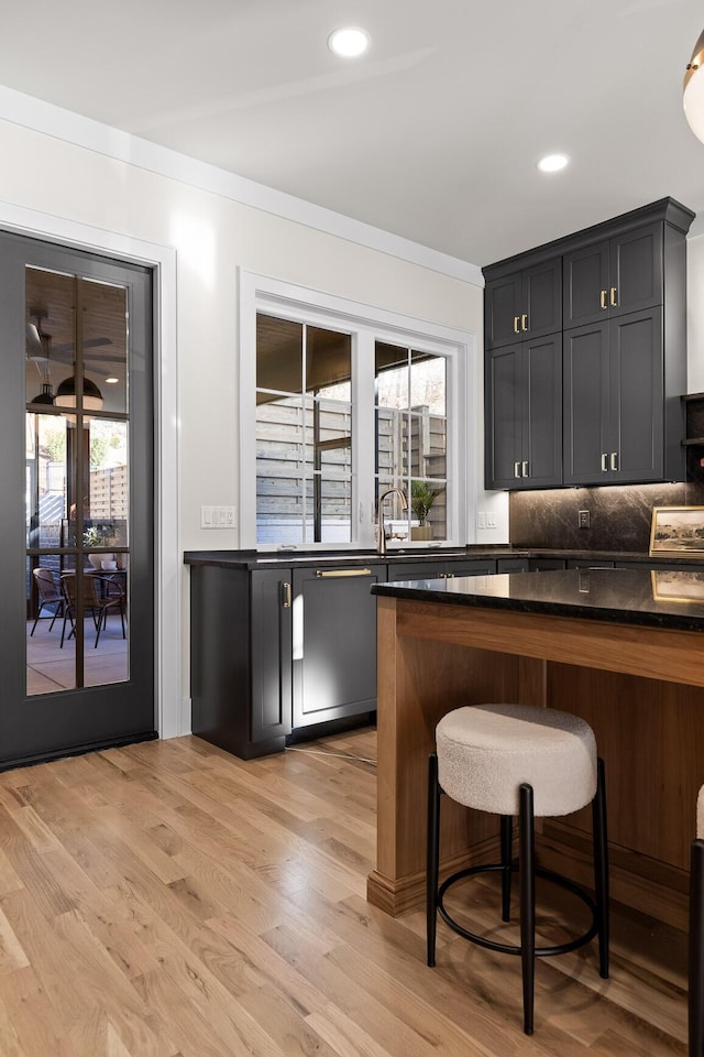 bar with light wood-type flooring, decorative backsplash, a sink, and recessed lighting