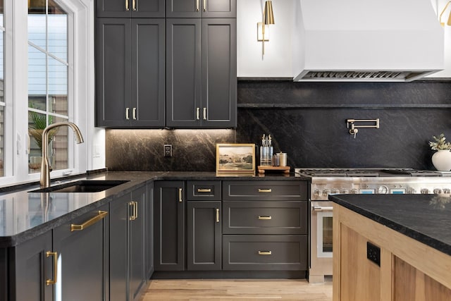 kitchen with decorative backsplash, dark stone counters, custom exhaust hood, stainless steel stove, and a sink