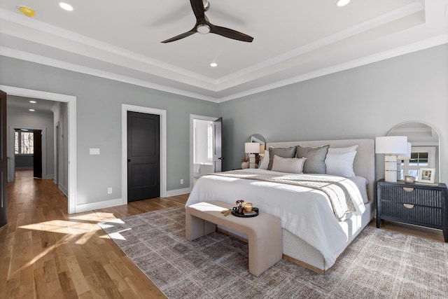 bedroom featuring baseboards, a raised ceiling, wood finished floors, crown molding, and recessed lighting