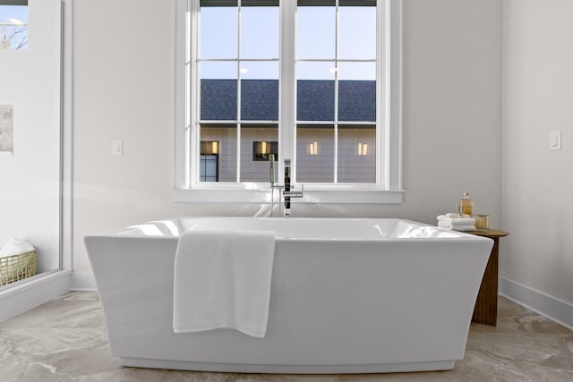 bathroom with a freestanding bath, marble finish floor, and baseboards