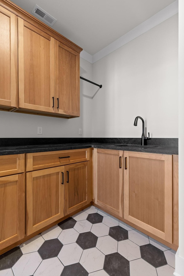 kitchen with ornamental molding, dark countertops, visible vents, and a sink