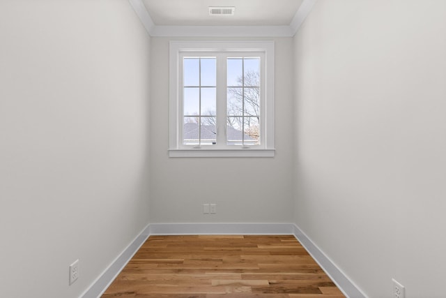 empty room featuring light wood-type flooring, baseboards, visible vents, and ornamental molding