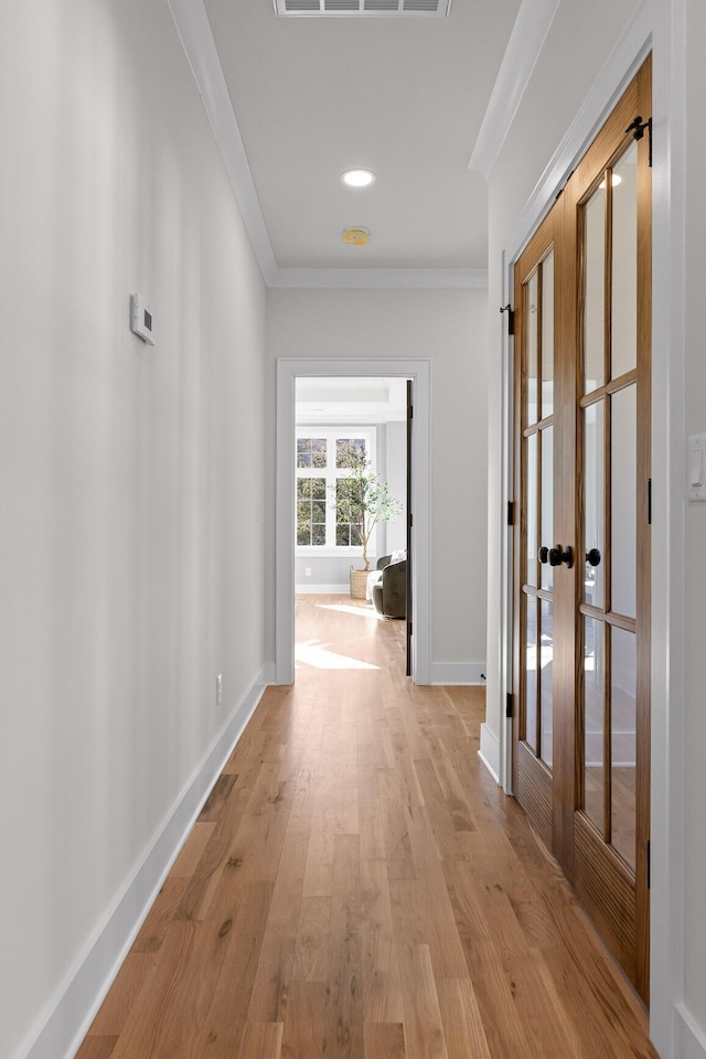 hall featuring light wood finished floors, ornamental molding, visible vents, and baseboards