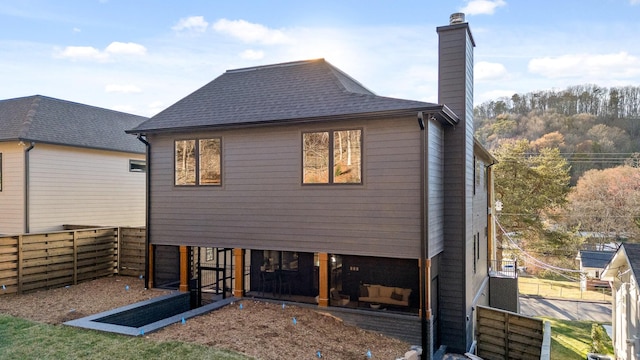 rear view of house featuring roof with shingles, a chimney, and a fenced backyard