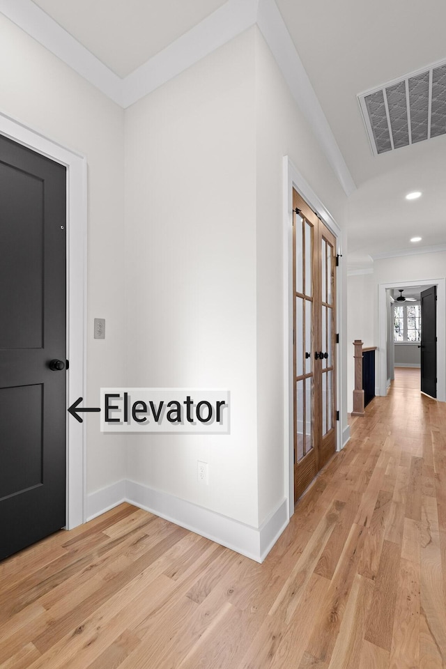 hallway with light wood-style floors, visible vents, ornamental molding, and baseboards