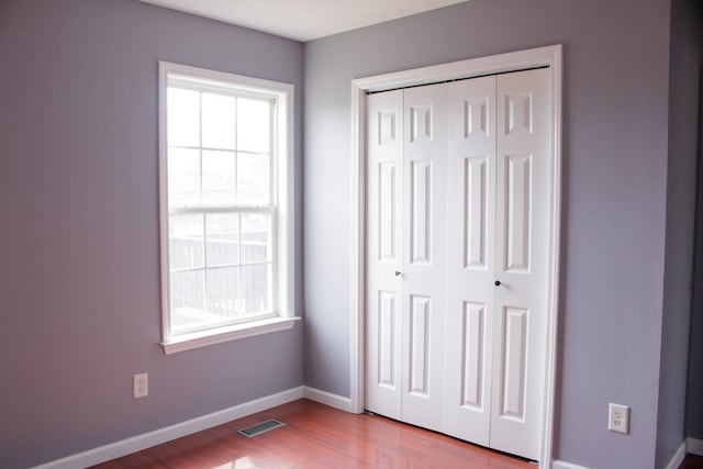 unfurnished bedroom with a closet, visible vents, baseboards, and wood finished floors