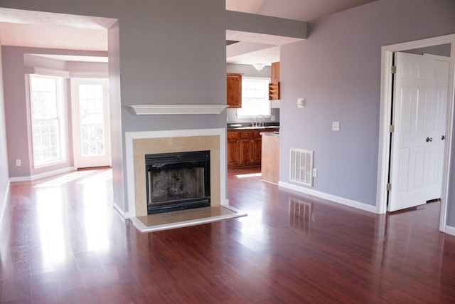 unfurnished living room featuring a wealth of natural light, visible vents, baseboards, and wood finished floors