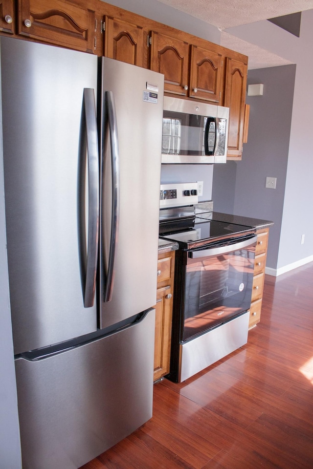 kitchen featuring dark wood-style floors, baseboards, appliances with stainless steel finishes, and brown cabinets