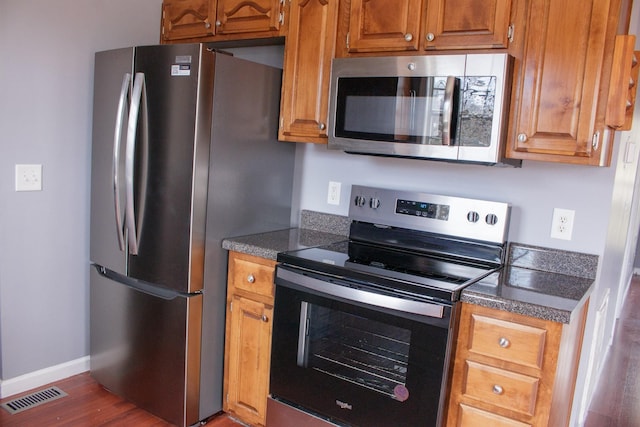 kitchen featuring appliances with stainless steel finishes, dark countertops, brown cabinets, and visible vents