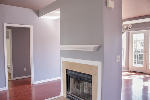 unfurnished living room with a notable chandelier, a fireplace, baseboards, and wood finished floors