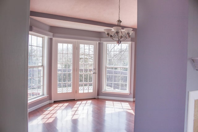 unfurnished dining area featuring baseboards, a chandelier, and wood finished floors