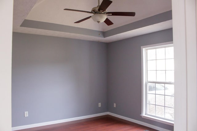 empty room featuring dark wood-style flooring, a raised ceiling, ceiling fan, and baseboards