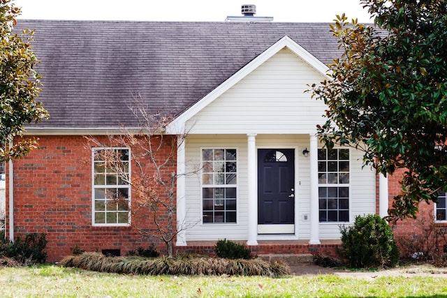 view of front facade featuring brick siding, a chimney, and roof with shingles