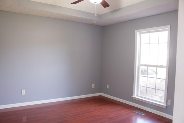 spare room with a raised ceiling, visible vents, dark wood finished floors, and baseboards