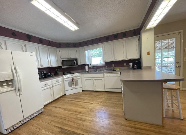 kitchen with a peninsula, white appliances, a sink, white cabinets, and light wood-style floors