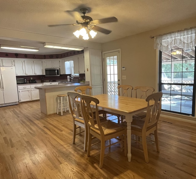 dining area with a textured ceiling, ceiling fan, and light wood-style floors