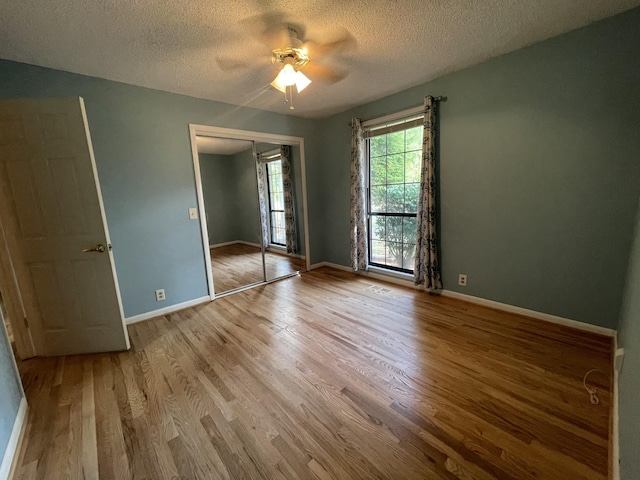 unfurnished bedroom featuring a closet, ceiling fan, a textured ceiling, wood finished floors, and baseboards