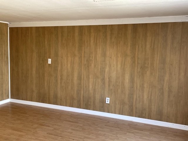 empty room featuring wood walls, wood finished floors, and baseboards