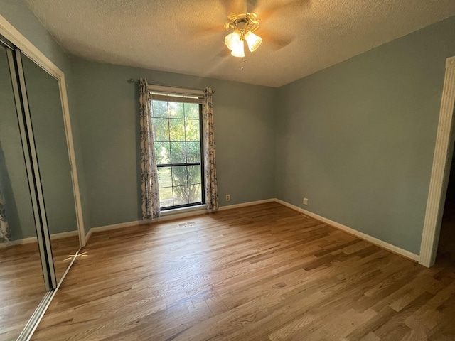 unfurnished bedroom featuring a closet, a textured ceiling, baseboards, and wood finished floors