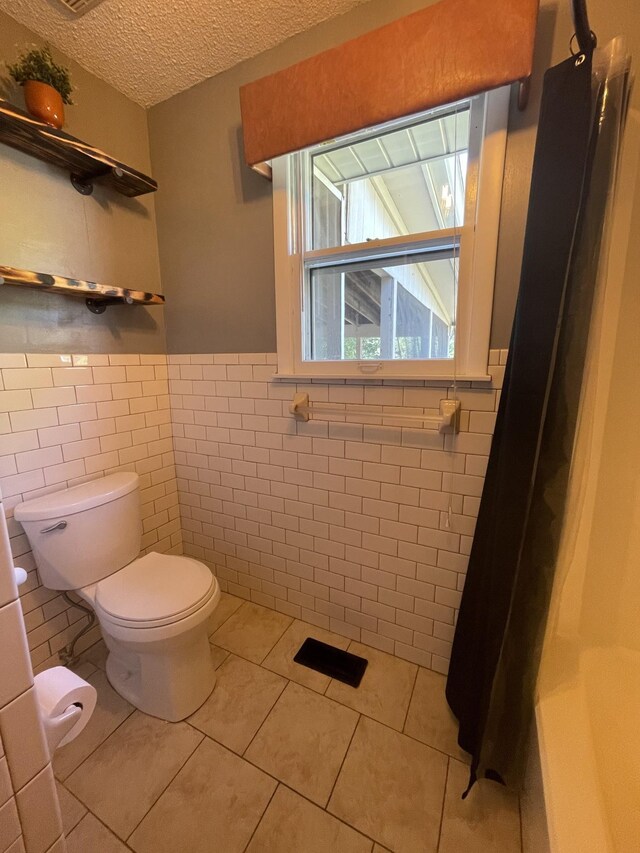 bathroom with a textured ceiling, toilet, a wainscoted wall, tile walls, and tile patterned floors