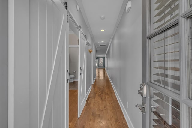 corridor with a barn door, baseboards, wood finished floors, and recessed lighting