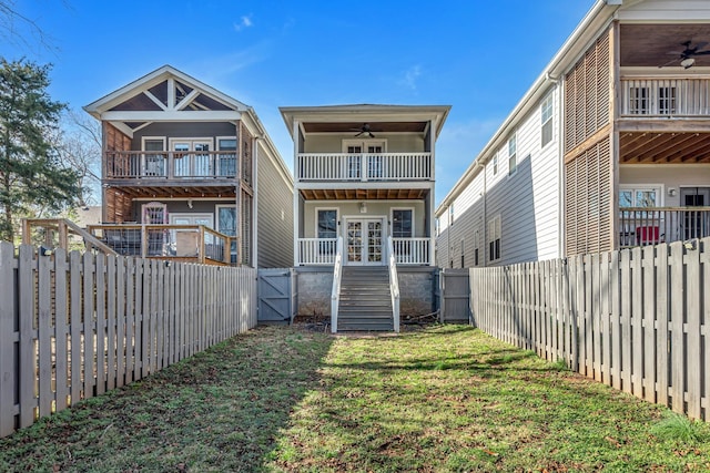 rear view of property featuring a ceiling fan, a fenced backyard, a lawn, and a balcony