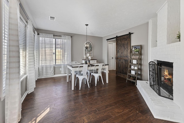 dining room with a barn door, visible vents, dark wood finished floors, and a fireplace