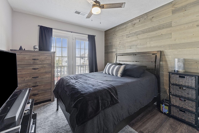 bedroom featuring visible vents, wood walls, wood finished floors, a textured ceiling, and a ceiling fan