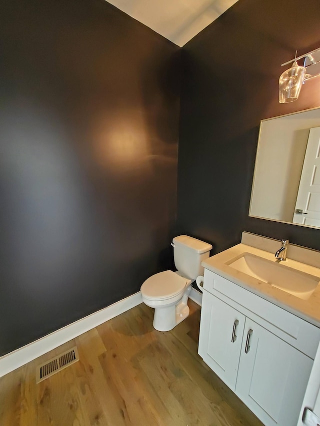 bathroom with toilet, wood finished floors, vanity, visible vents, and baseboards