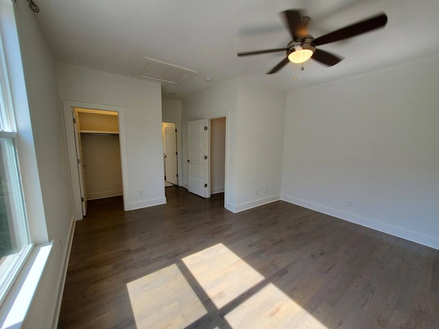 unfurnished bedroom with dark wood-style flooring, a ceiling fan, baseboards, a spacious closet, and attic access