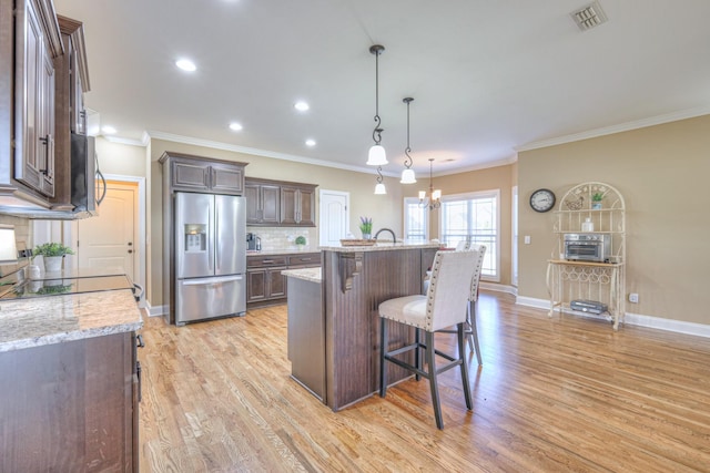 kitchen featuring appliances with stainless steel finishes, visible vents, dark brown cabinets, and a kitchen breakfast bar